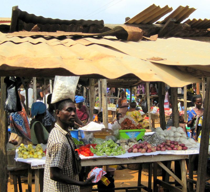 A man balancing a bag on his head in a Ghanaian market.
