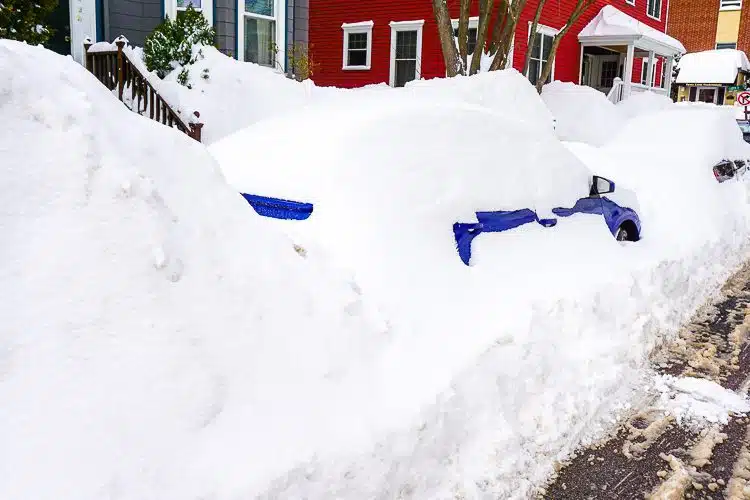 A blue car peeking out of the snow bank. 