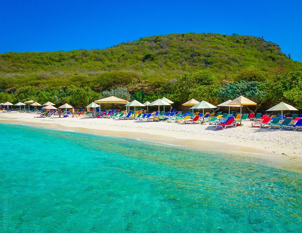The beach at Porto Mari features crystal water and rainbow chairs.