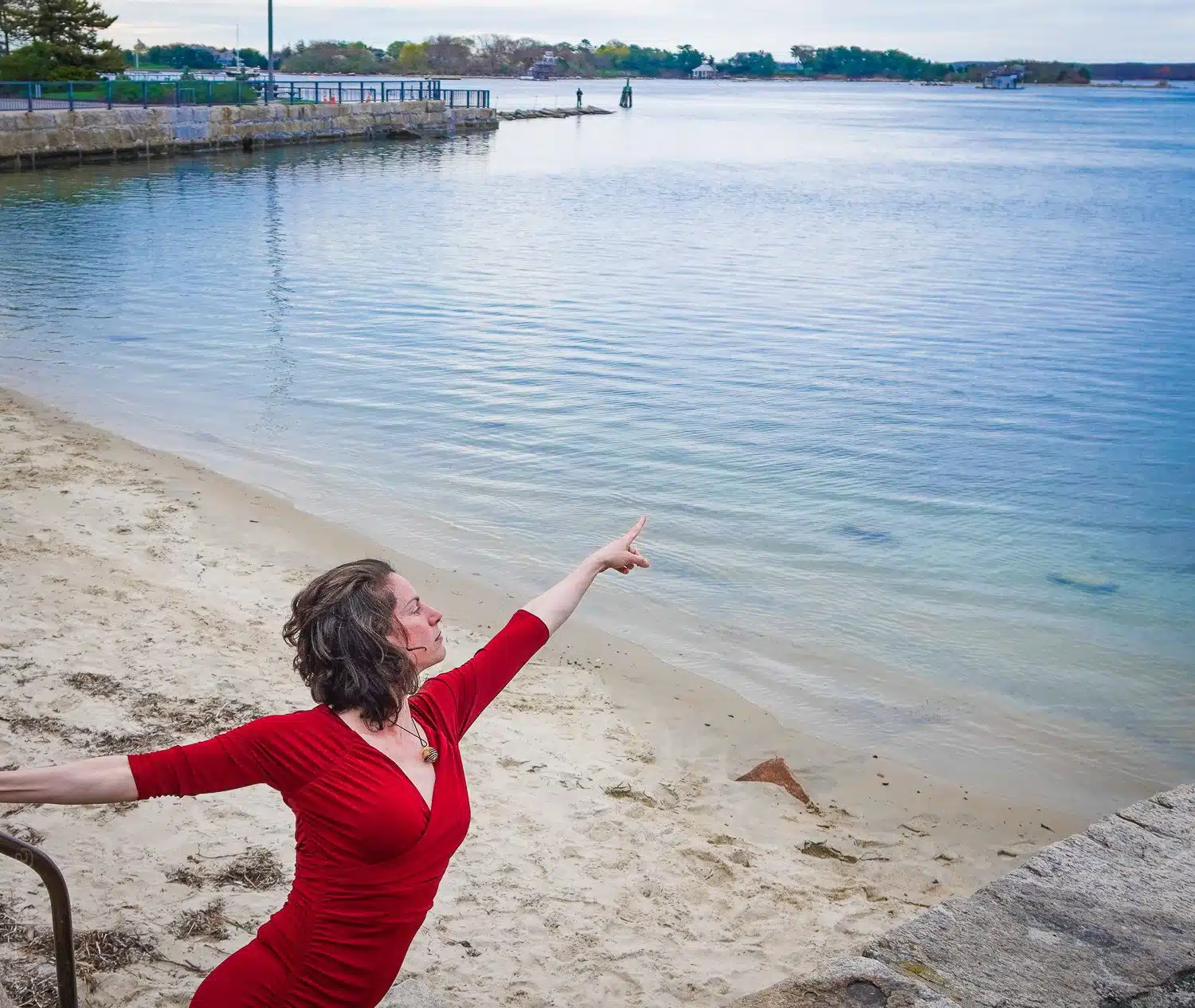 Pointing at Woods Hole beach in a red dress